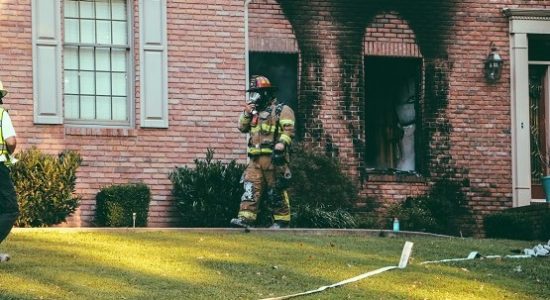 Feuerwehrmann vor einem verrußtem Haus