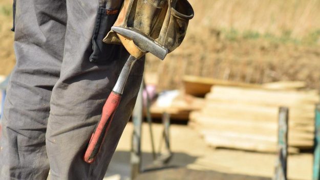 Beine eines Bauarbeiters mit Hammer an der Werkzeugtasche