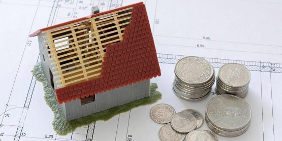 Modell eines Hauses mit einigen Stapeln Geldmünzen auf einer Hausskizze
