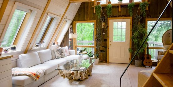 Hell eingerichteter Dachboden, mit Sofa, Glastisch, Gitarre und Pflanzen an den Wänden