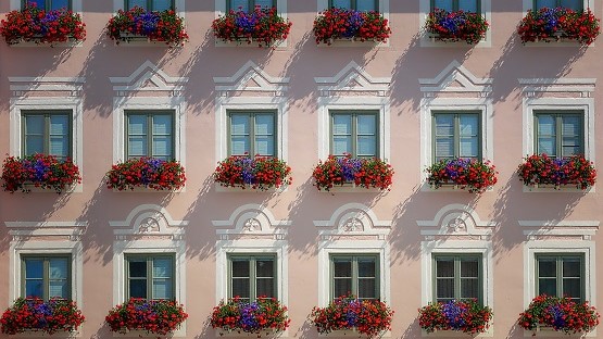 Hauswand mit Fensterreihen und Blumen in den Balkonkästen