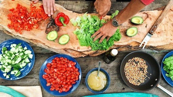 Salate, Paprika und weitere Zutaten werden auf Holzplatte einer Gartenküche vorbereitet.