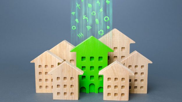 Ein grünes Modell eines Hauses aus Holz zwischen sechs naturbelassenen Holzhausmodellen in verschiedenen Größen