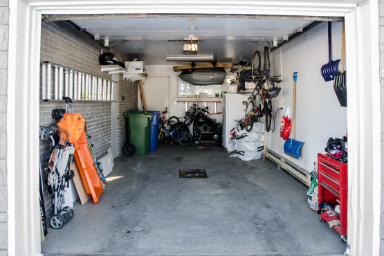 Blick in eine offene Garage auf Fahrräder, Mülltonen und andere Gegenstände.