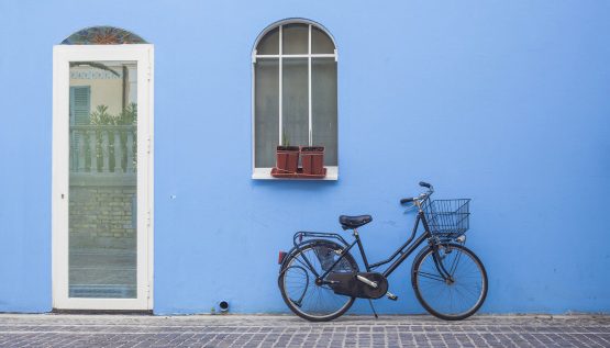 Blaue Fassade mit weißer Tür und Fahrrad davor