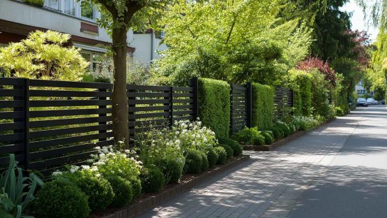 Ein moderner, schwarzer Zaun um einen Garten. Zwischen den Zaunteilen stehen einige Heckenelemente