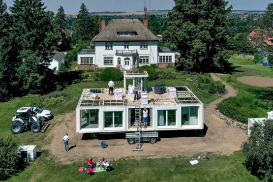 Montage eines modularen Wohngebäudes aus vorgefertigten Raummodulen auf einer Baustelle mit Kran und Montageteam