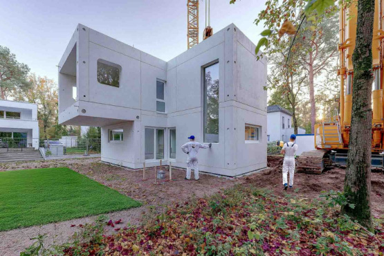 Modernes Modulhaus aus vorgefertigten Betonelementen während der Montage auf einer Baustelle mit Kran und Monteuren
